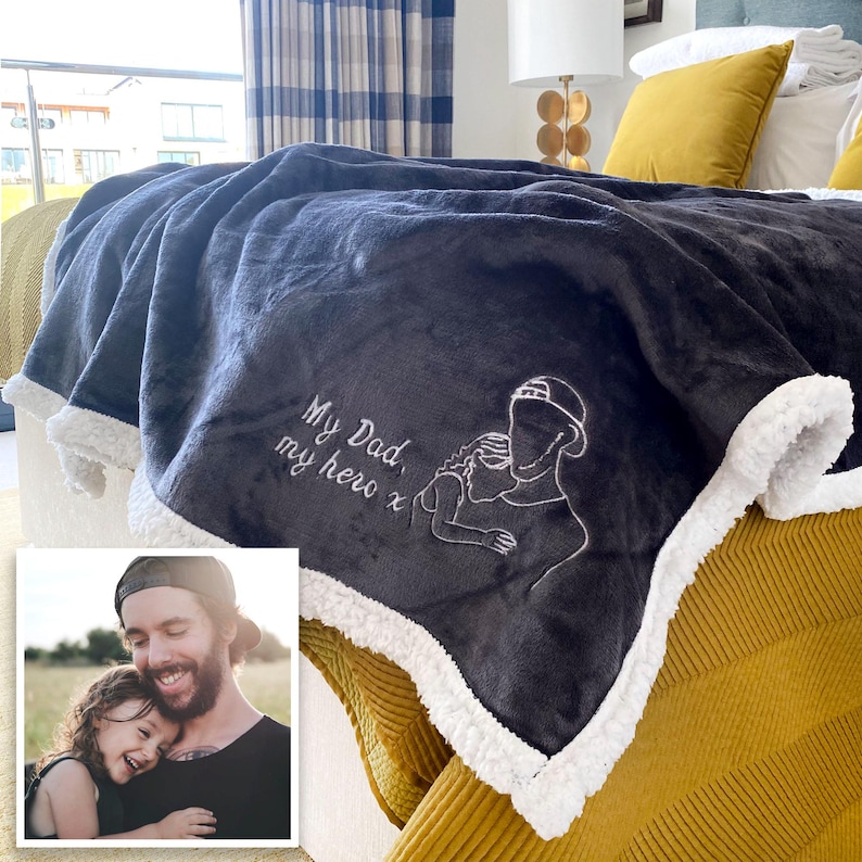 Pode incluir: Uma manta de l&atilde; cinza com uma borda de sherpa branca. A manta tem um desenho bordado de um pai e uma crian&ccedil;a com o texto "My Dad, my hero x".