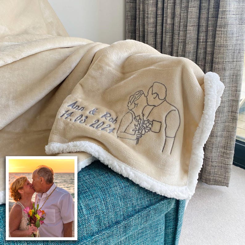 Pode incluir: Uma manta de l&atilde; de carneiro bege com uma borda de sherpa branca. A manta tem um design bordado personalizado de um casal se beijando com o texto "Ann & Rob 14.03.2024".