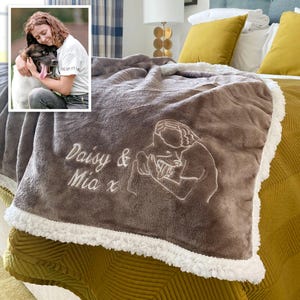 May include: A brown fleece throw blanket with a white sherpa border. The blanket is embroidered with a line drawing of a person holding a dog and the text "Daisy & Mia x".
