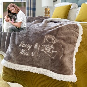 Pode incluir: Uma manta de l&atilde; marrom com uma borda de sherpa branca. A manta &eacute; bordada com um desenho de linha de uma pessoa segurando um cachorro e o texto "Daisy & Mia x".