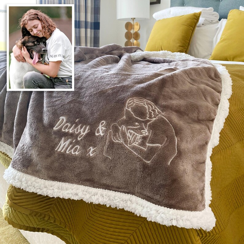 Pode incluir: Uma manta de l&atilde; marrom com uma borda de sherpa branca. A manta &eacute; bordada com um desenho de linha de uma pessoa segurando um cachorro e o texto "Daisy & Mia x".