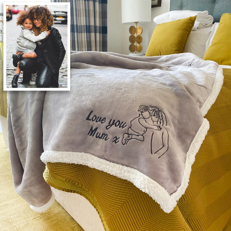 Pode incluir: Uma manta de l&atilde; cinza com uma bainha de sherpa branca. A manta tem um desenho bordado de uma m&atilde;e e uma crian&ccedil;a com o texto "Love you Mum x".