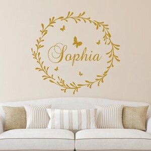 May include: Gold vinyl wall decal with a leafy wreath and the name "Sophia" in a cursive font.  Five small butterflies are scattered around the wreath.