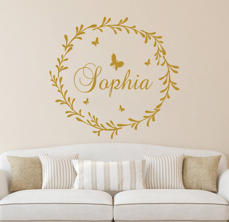 May include: Gold vinyl wall decal with a leafy wreath and the name "Sophia" in a cursive font.  Five small butterflies are scattered around the wreath.