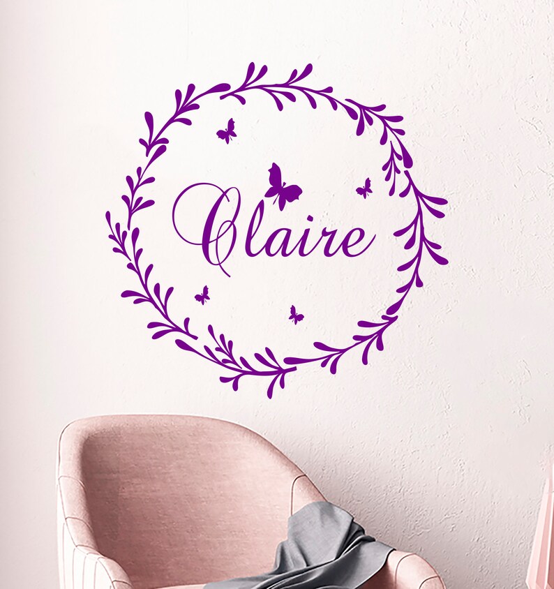 May include: Purple vinyl wall decal with a floral wreath and the name "Claire" in a cursive font. Five small butterflies are scattered around the wreath.