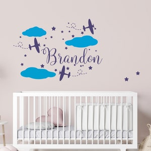 May include: A nursery wall decal with the name "Brandon" written in a cursive font. The decal features blue clouds, stars, and airplanes.