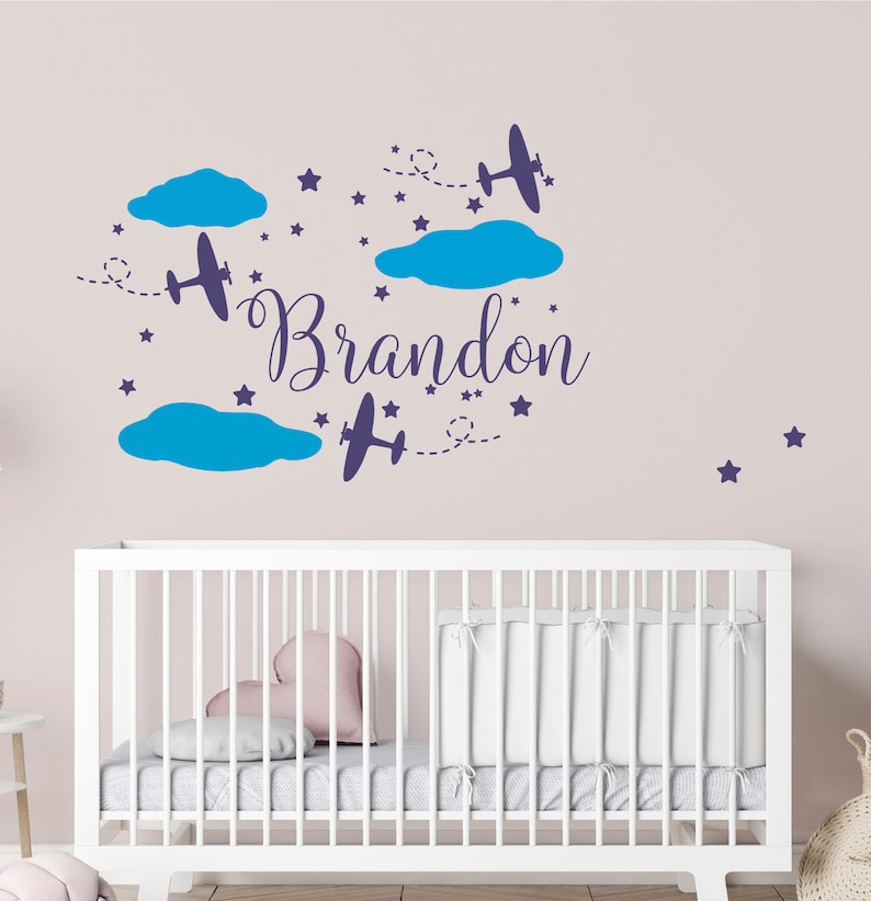 May include: A nursery wall decal with the name "Brandon" written in a cursive font. The decal features blue clouds, stars, and airplanes.