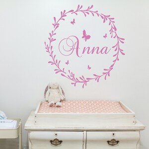 May include: Pink floral wreath wall decal with the name "Anna" in a cursive font and several small butterfly silhouettes.