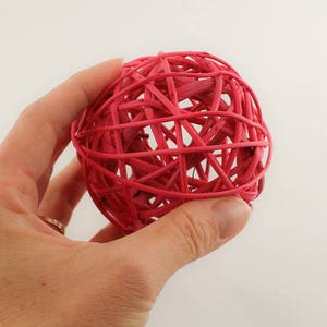 May include: A pink woven ball ornament with a decorative, intricate design. The ball is made of thin, interwoven strands of material.