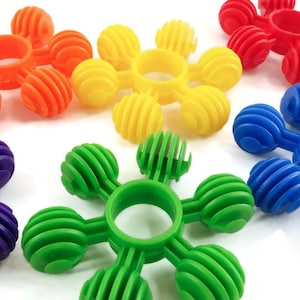 May include: Five colorful plastic toys shaped like flowers with six rounded petals and a center ring. The toys are orange, yellow, red, blue, and green.