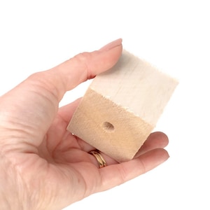 May include: A small, light brown wooden block with a hole in the center. The block is smooth and has a slightly rough texture.