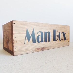 May include: A wooden box with the words "Man Box" printed in black on the front.