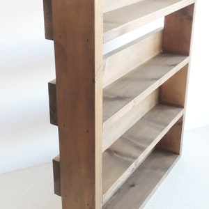 May include: A rustic wooden shelf unit with four shelves. The shelf is made of natural wood with a dark brown stain. The shelf is freestanding and has a rectangular shape.