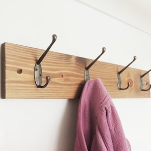 May include: A wooden coat rack with four hooks, painted in a dark brown stain. A pink jacket is hanging on one of the hooks.