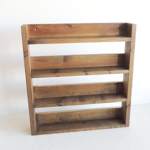 May include: A rustic wooden spice rack with five shelves. The rack is made of unfinished wood with a dark brown stain. It is mounted on a white wall.