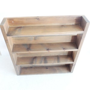 May include: A rustic wooden shelf unit with four shelves. The shelf is made of natural wood with a brown stain. The shelf is mounted on a wall.