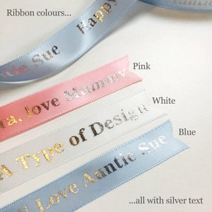 K&ouml;nnte beinhalten: Nahaufnahme von farbigen B&auml;ndern mit silbernem Text. Die B&auml;nder sind in verschiedenen Farben wie Rosa, Wei&szlig; und Blau gehalten und tragen Aufschriften wie "Happy" und "Love Mummy". Das Bild enth&auml;lt auch den Text "Ribbon colours..." und "...all with silver text."