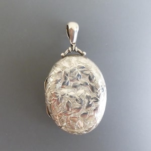 Peut inclure: Pendentif ovale argenté avec un motif floral. Le pendentif est doté d'une boucle pour une chaîne et d'une ouverture à charnière. Le motif floral recouvre toute la face avant du médaillon.