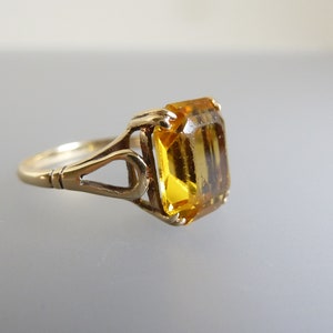 May include: A gold ring with an emerald-cut yellow gemstone set in an intricate, openwork design.