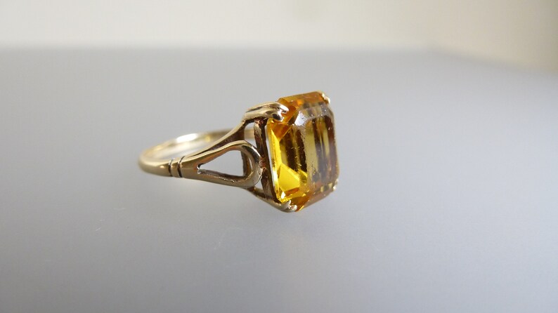 May include: A gold ring with an emerald-cut yellow gemstone set in an intricate, openwork design.