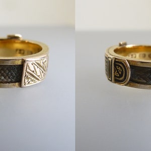 Puede incluir: Un anillo de banda de oro con paneles alternos de patrones geom&eacute;tricos grabados y secciones de incrustaciones oscuras y texturizadas. El interior de la banda muestra sellos visibles y el dise&ntilde;o incluye un peque&ntilde;o mecanismo de cierre en el borde.