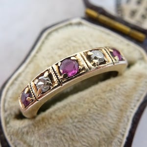 May include: A gold band ring with five ruby and diamond stones set in a decorative design. The ring is in a small velvet-lined box.