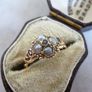 以下が含まれることがあります： 真珠と赤い宝石のクラスターが付いた金の指輪。指輪はベルベットの指輪箱に入っています。