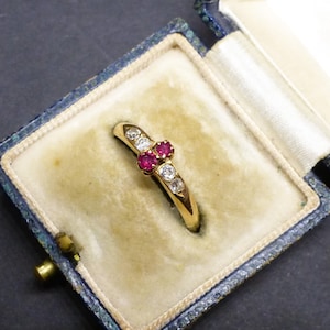 Peut inclure: Une bague en or ornée de deux rubis rouges ronds centraux, flanqués de deux diamants ronds transparents de chaque côté, présentée dans un écrin à bijoux doublé de velours bleu avec du texte imprimé sur le couvercle intérieur, incluant Dundee.