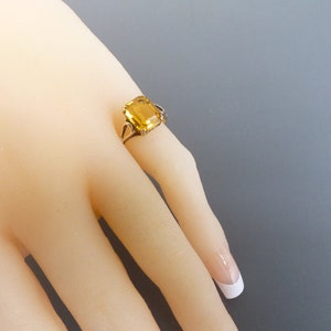 May include: A gold ring with a large, square-shaped, yellow gemstone.