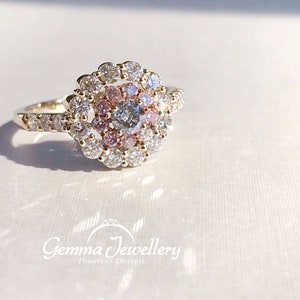 May include: A gold ring with a center diamond surrounded by a halo of smaller diamonds. The halo is set with pink diamonds in a swirling pattern.