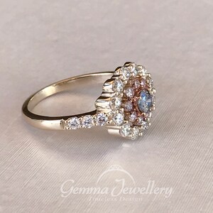 May include: A silver ring with a large, round, blue and pink gemstone surrounded by smaller diamonds. The ring has a delicate band with smaller diamonds set along the side.
