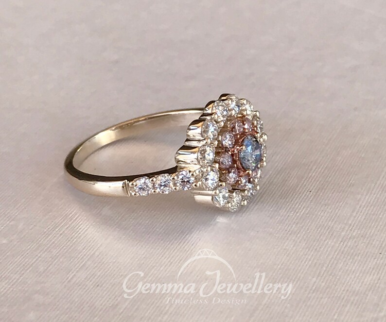 May include: A silver ring with a large, round, blue and pink gemstone surrounded by smaller diamonds. The ring has a delicate band with smaller diamonds set along the side.