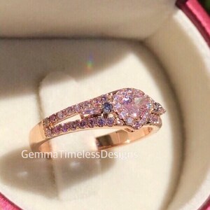 May include: A rose gold ring with a heart-shaped pink gemstone surrounded by smaller pink gemstones. The ring has a double band with a row of smaller pink gemstones on each band.