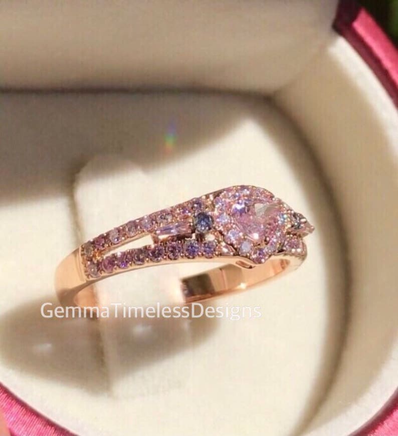 May include: A rose gold ring with a heart-shaped pink gemstone surrounded by smaller pink gemstones. The ring has a double band with a row of smaller pink gemstones on each band.