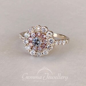 May include: A silver ring with a large, round, multi-faceted center stone surrounded by a halo of smaller stones. The halo is made up of three rows of stones, with the inner row being pink, the middle row being white, and the outer row being clear. The ring band is also set with small, clear stones.