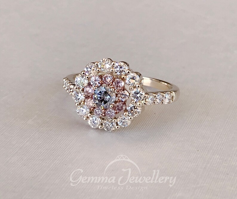 May include: A silver ring with a large, round, multi-faceted center stone surrounded by a halo of smaller stones. The halo is made up of three rows of stones, with the inner row being pink, the middle row being white, and the outer row being clear. The ring band is also set with small, clear stones.