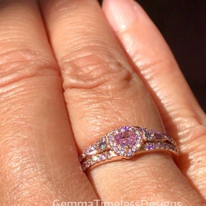 May include: A rose gold ring set with a heart-shaped pink gemstone surrounded by smaller diamonds. The ring is on a finger.