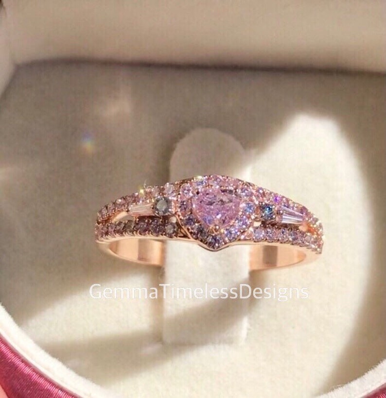 May include: A rose gold ring with a heart-shaped pink gemstone surrounded by smaller diamonds. The ring has a double band with additional diamonds.