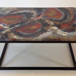 May include: A coffee table with a black metal frame and a colorful resin top. The resin top features swirling patterns of red, blue, gold, and white.