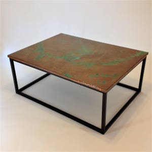 May include: A modern coffee table with a copper top and a black metal frame. The copper top has a green patina finish.