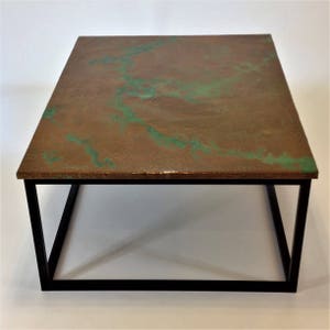 May include: A square coffee table with a copper top and a black metal frame. The copper top has a green patina finish.