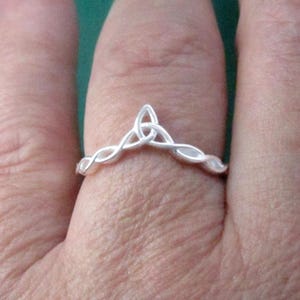 May include: A silver ring with a Celtic knot design. The ring is worn on a finger.