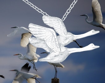 May include: A silver-toned necklace featuring a stylized design of two birds in flight, with a chain. The background shows several white birds in flight against a blue sky.