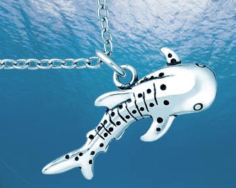 May include: A silver-toned whale shark pendant suspended from a matching metal link chain. The pendant features a detailed, three-dimensional design of a whale shark with prominent black spots and stripes along its body and fins.