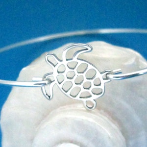 May include: A silver bangle bracelet with a cutout turtle charm. The turtle has a detailed shell design.