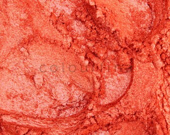 May include: Close-up of a bright orange powder with a shimmery, metallic finish. The powder is textured and has a fine, granular consistency.