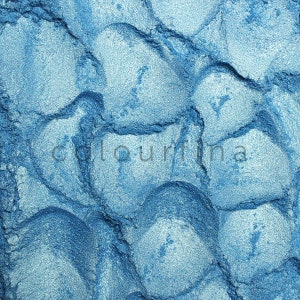 May include: Close-up of a blue metallic powder with a textured surface. The powder has a shimmery finish and is perfect for creating a variety of makeup looks.