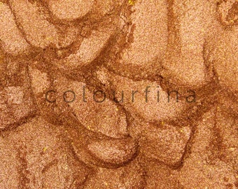 May include: Close-up of a metallic bronze eyeshadow with a shimmery finish. The eyeshadow has a textured, swirled appearance.