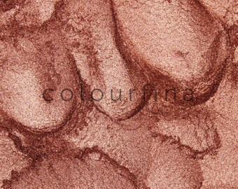 May include: Close-up of a metallic, shimmery, copper-colored eyeshadow. The eyeshadow has a fine, glittery texture.