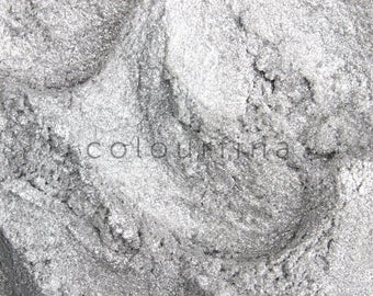 Puede incluir: Primer plano de un polvo plateado brillante con una apariencia texturizada y granulada. El polvo tiene un brillo metálico, con áreas de luz y sombra. La palabra "colourina" está impresa en blanco en la imagen.